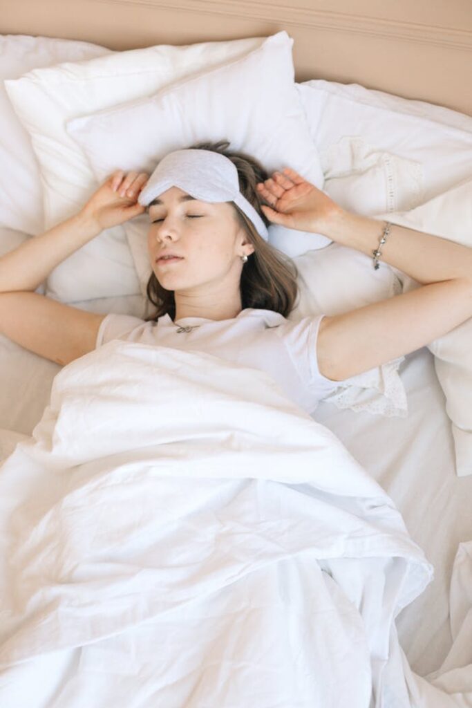 A woman sleeping soundly in bed with a white eye mask and cozy linens for a restful night.